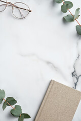 Canvas Print - Creative workspace with paper notebook, glasses, eucalyptus leaves on marble background. Minimal style home office desk table. Flat lay, top view.