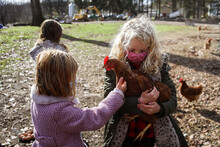 Girl With Blonde Hair Holding Chicken On A Farm