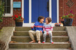 © Cavan Images - A brother and sister sit smiling together on front stoop of home