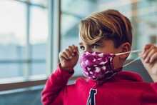 Young Boy Wearing A Mask Close To A Window At Airport, Fixes Own Mask.