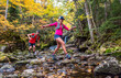 © Cavan Images - Man and woman trail runners rock-hopping in a river with fall foliage