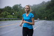 © Cavan Images - Athletic woman running along road on wet summer day