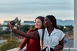 © Cavan Images - Two young women are taking a self-portrait with their phone at sunset
