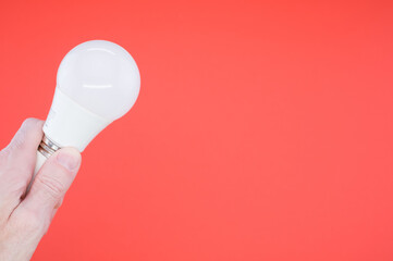 Sticker - Closeup shot of a hand holding a LED light bulb on a red background