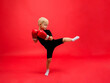 a little boy boxer stands sideways in red boxing gloves and makes a kick on a red background with space for text