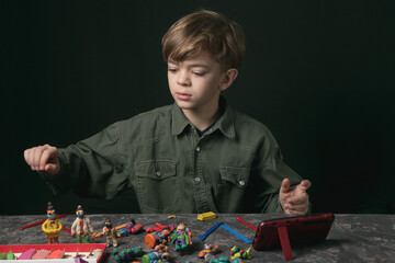 a little boy sits at a table and sculpts from plasticine