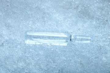 vaccine in a glass transparent ampoule with a medical preparation for the treatment of coronavirus disease chilled for transport temperature lying on cold ice background on a medical theme.