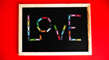 The Word Love Is Laid Out From Colorful Clips On A Black Board On A Red Background. The Concept Of Valentine's Day.