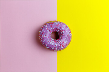 Donut with pink chocolate icing with multicolored sprinkles on a pink yellow background