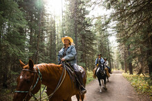 Happy Mature Women Friends Horseback Riding On Trail In Sunny Woods