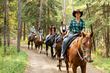 Female Rancher Leading Family On Horseback Ride On Trail In Woods
