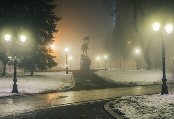 Poster - Silhouette of a monument to the January Uprising of 1918 in a night winter park in a fog with benches and latterns. Beautiful foggy evening in the Mariinsky Park. Kyiv, Ukraine.