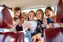 Playful Teenage Girl Friends Taking Selfie In Back Seat Of Car