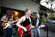 Teenage Girl Friends Singing And Playing Electric Guitar In Driveway