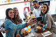 © nenetus - Happy group of friends taking selfie with smart phone while eating burgers in a restaurant.