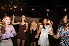 Portrait Happy Teenage Girl Friends Dancing With Sparklers In Backyard