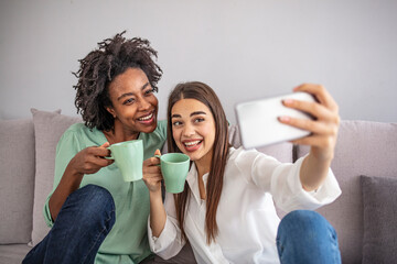 Wall Mural - Shot of a two female friends taking selfie in the apartment. My roomies. Shot of two young women taking a selfie while sitting at home. Shared Living: roommates make a selfie