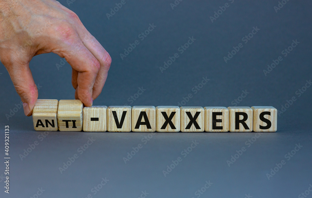 Anti-vaxxers symbol. Doctor turns cubes, changes words 'vaxxers' to 'anti-vaxxers'. Beautiful grey background. Copy space. Medical covid-19 vaxxers or anti-vaxxers concept.