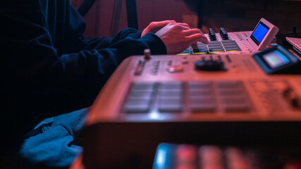 The hands of an artist creating music with his drum machines under red light.