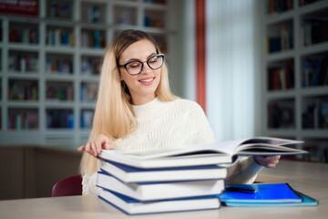 Portrait of clever student with open book reading it in college library.