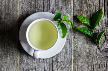 Wall Mural - White cup of green tea with fresh tea leaves on wooden table, hot drink concept