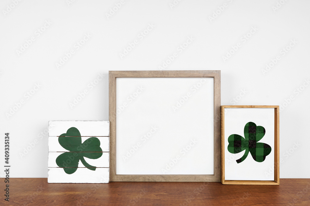 Mock up wood frame with St Patricks Day decor on a wood shelf. Rustic wood signs. Square frame against a white wall. Copy space. - obrazy, fototapety, plakaty 