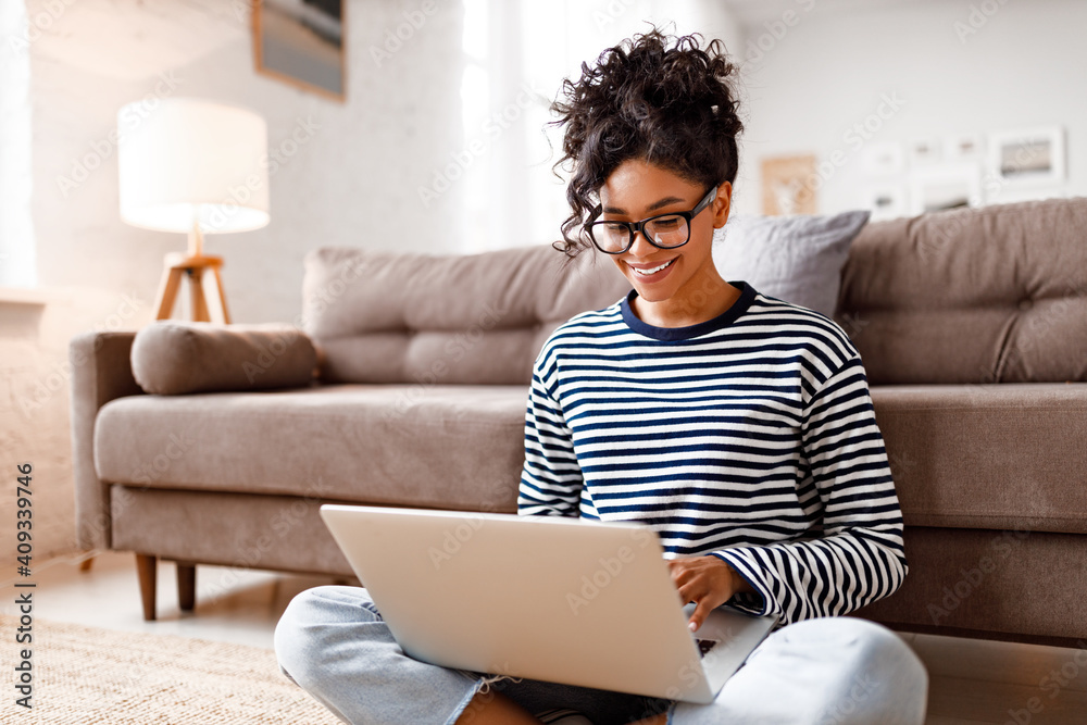 Joyful relaxed ethnic woman using laptop with interest at home - obrazy, fototapety, plakaty 