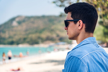 Wall Mural - Portrait of smiling happy handsome man model enjoying and relax in fashionable hipster summer sunglasses standing on the tropical beach and looking at sea.Summer vacations and travel