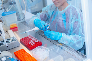 Dna test in the lab. a laboratory technician with a dispenser in his hands is conducting dna analysis in a sterile laboratory behind glass