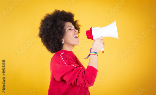 Angry brave young African woman standing on black background raising fist and screaming. Mixed race lady activist feminist leader fighting for women rights,