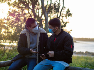 Friends with face masks talking in a park at sunset - concept of the new normal