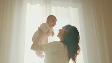 young happy mother holds an adorable infant in her hands and lifts her up. mom plays with daughter i