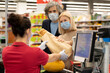 © pressmaster - Mature man and woman in protective masks passing packet with bread to cashier