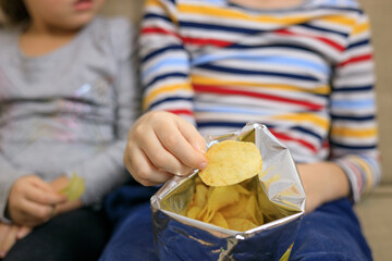 Boy and girl sitting on sofa, eating chips from packet