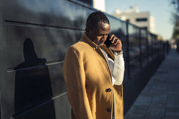 Wall Mural - Shallow focus shot of a stylish handsome African male in a coat talking by phone