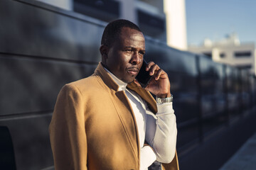 Wall Mural - Shallow focus shot of a stylish handsome African male in a coat talking by phone