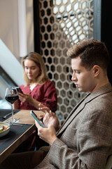 Wall Mural - Young serious man and woman in smart casualwear scrolling in their smartphones