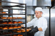 © salomonus_ - Baker takes out a baking tray with hot pastries from a cart on the background of an industrial oven.