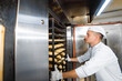 © salomonus_ - baker boy inserts a cart with raw dough baking trays into an industrial oven in a bakery.