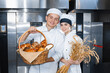 © salomonus_ - bakers boy and girl with a baking basket and spikelets of wheat against the background of an industrial oven in a bakery.