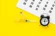 Leinwandbild Motiv Glass medicine vial with liquid and syringe, calendar and alarm clock on yellow background. Medical vassination schedule. Health concept. Flat lay, top view with copy space.