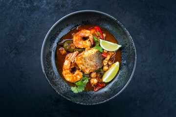 Wall Mural - Modern style traditional Mexican seafood pozole soup with fish, king prawns and hominy in a clear sauce served as top view in design bowl