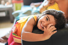 Happy Indian Child Having Fun Sitting On Sofa With Parents At Home - Focus On Girl
