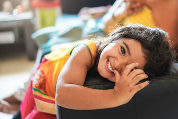 Wall Mural - happy indian child having fun sitting on sofa with parents at home - focus on girl