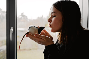 portrait of teen girl playing with her rat pet in front of window. pets and children friendship conc