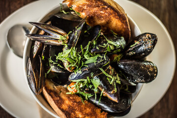 Fresh mussels with tomato, fresh chilli, parsley, grilled bread in small white bowl