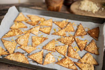 Process of cooking cheese Tortilla chips with olive oil on baking sheet before oven, homemade salty savory pastry snack in the kitchen. Selective focus with copy space.