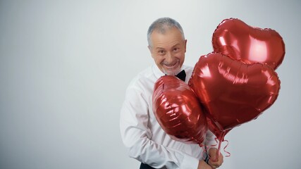 Wall Mural - A funny old man with a beard with red balloons in the form of hearts is dancing