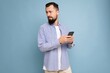 © Ivan Traimak - Thoughtful handsome young man isolated over background wall wearing everyday clothes holding and using mobile phone writing sms looking to the side and thinking