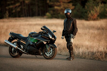 Motorcycle Driver In A Helmet And Leather Jacket Stands On The Road Next To A Sports Motorcycle